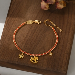 Detailed view of woven red string bracelet with gold horse, coin and heart pendants
