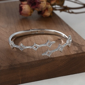 Elegant silver open bangle with pavé zircon star patterns on a wooden display stand