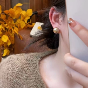Close-up of champagne gold pearl stud earring worn with a cozy autumn knit sweater