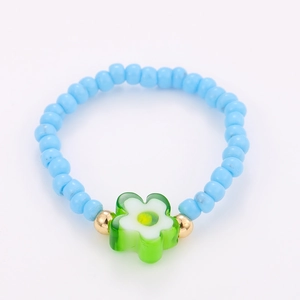 Detail of light blue beaded ring featuring a green flower charm and golden spacers