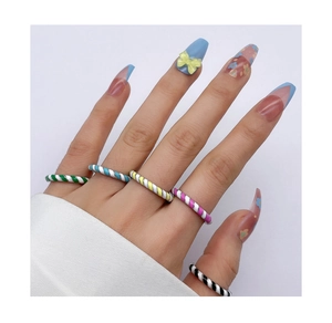 Dettaglio di un set di anelli a spirale in smalto colorato indossati su dita con smalto vivace