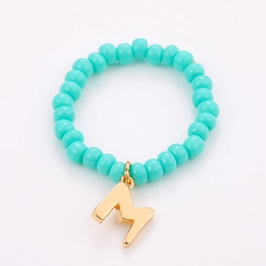 Detail of turquoise seed bead ring featuring a polished gold metal letter M charm