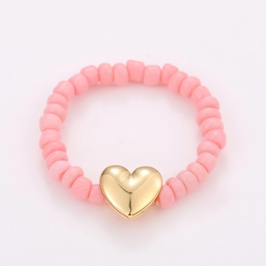 Detail of pink matte beads and a polished golden heart pendant on a stylish stretch ring