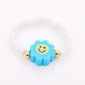 Detail of beaded ring featuring white beads, gold accents, and a blue smile flower design