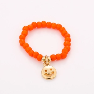 Detail of colorful beaded ring with orange beads and a golden smiling face pendant
