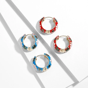 Detailed macro of enamel hoop earrings with floral patterns on a white podium