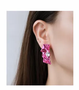 Detailed close-up of metallic pink wrinkled earrings with clear central crystal on a model
