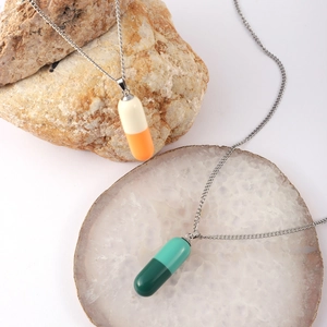 Detalle de colgantes de cápsula de resina bicolor en cadenas plateadas sobre piedra natural