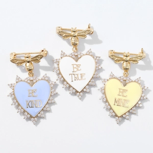 Detailed close-up of heart enamel pins with gold bees and BE KIND BE TRUE BE MINE text