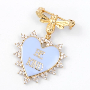 Golden bee brooch with light blue enamel heart and Be Kind lettering on white background