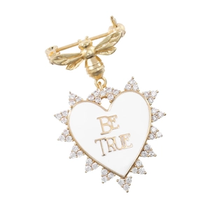 Detail view of gold bee brooch with a white enamel heart pendant and BE TRUE engraving