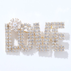 Spilla dorata con lettere LOVE, strass scintillanti e un piccolo fiore bianco per San Valentino