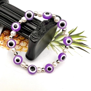 Dettaglio macro delle perline viola malocchio e perle bianche sul bracciale elastico boho
