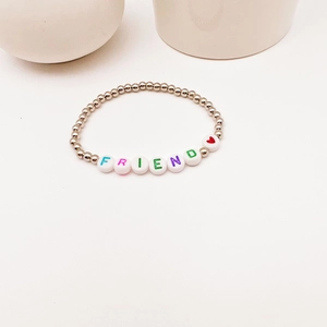 Détail d'un bracelet en perles argentées et perles de lettres FRIEND sur fond blanc
