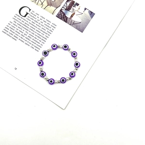 Dettaglio macro del braccialetto elastico Evil Eye con perle in resina viola su rivista