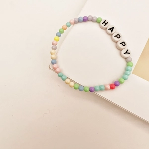Gros plan d'un bracelet en perles colorées avec perles HAPPY aux tons macarons