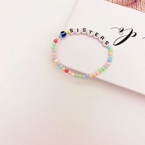 Détail du bracelet en perles colorées avec lettrage Sisters et breloque œil bleu
