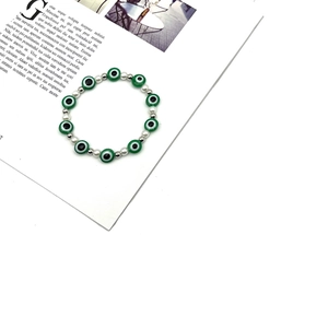 Braccialetto malocchio con perle bianche e ciondoli verdi su sfondo di una rivista