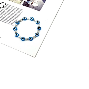 Bracciale di perle con occhio greco blu e accenti argentati su sfondo bianco elegante