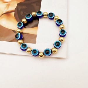 Dettaglio delle perle blu Evil Eye e delle sfere di metallo dorato lucido su bracciale elastico