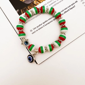 Detail showing the Evil Eye Hamsa Hand charm on a red, white, and green beaded bracelet