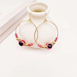 Gold evil eye hoop earrings with red beads and rhinestones on a ceramic stand