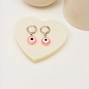 Minimalistische silberfarbene Evil-Eye-Ohrhänger mit rosa Perlen auf einer weißen Marmorplatte
