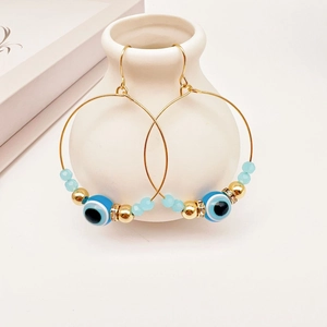 Golden hoop earrings with evil eye beads and crystal spacers on a white vase