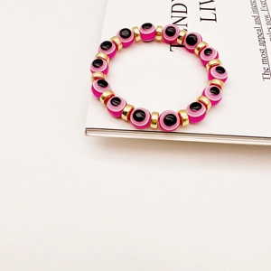 Turkish pink evil eye beaded bracelet with gold cylindrical spacers on white magazine