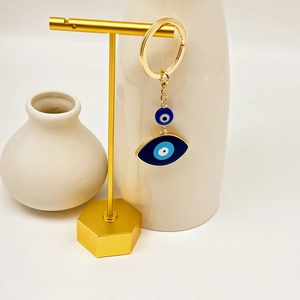 Golden Evil Eye keychain with blue beads on a premium minimalist jewelry display stand