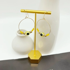 Detail of gold evil eye hoop earrings with yellow beads on a T-shaped metal display stand