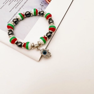 Detail of Hamsa Hand and Evil Eye charm on a red, white, and green beaded elastic bracelet