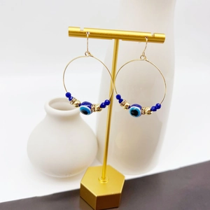 Detail of gold evil eye hoop earrings with blue glass beads on a hexagon jewelry stand