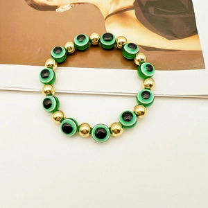 Dettaglio delle perline verdi Evil Eye e sfere metalliche dorate sul bracciale elastico
