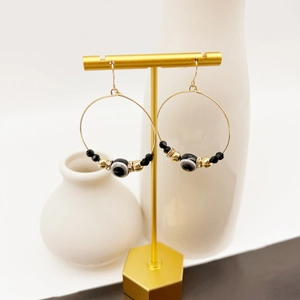 Close-up of gold hoop earrings with evil eye beads and black charms on a metal stand