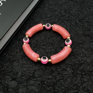 Evil eye bracelet with pink marble tubes and golden beads on a black background