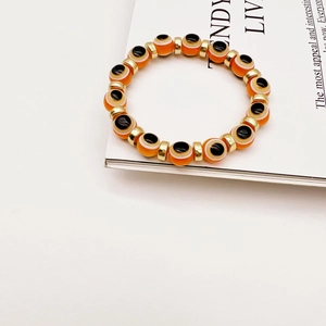 Detailed close-up of orange Evil Eye beaded bracelet with golden metal spacers on a magazine