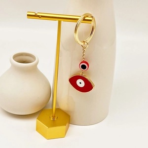 Detail of golden Evil Eye keychain with two red enamel charms on a display stand