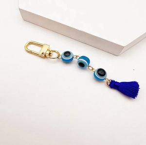 Gold Evil Eye keychain with blue glass beads and silk tassel on a clean white background