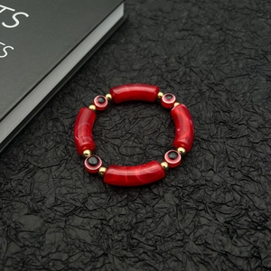 Evil Eye beaded bracelet with red marble resin tubes and golden accents on black background