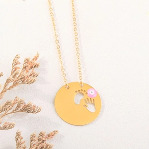 Detalle del collar dorado con colgante de huellas de bebé y amuleto de ojo turco rosa