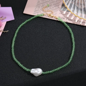 Détail d'un collier de perles vert clair avec perle baroque blanche et fermoir doré