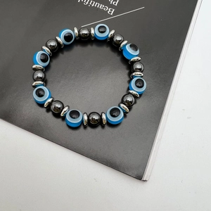 Elastic bracelet with blue evil eye beads and dark grey hematite stones on a minimal background