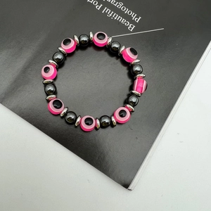 Macro detail of elastic bead bracelet with pink evil eye charms and hematite stones
