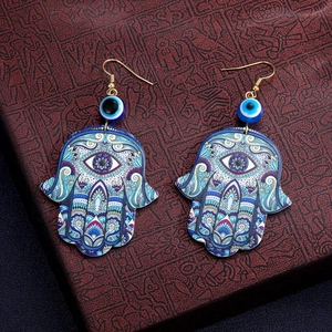 Makroaufnahme von Hamsa-Hand-Ohrringen mit blauen bösen Augenperlen und Mandala