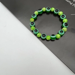 Detailed macro view of green evil eye and agate patterned beads on an elastic bracelet