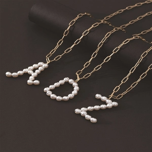 Detail of A D Z pearl letter pendants on golden paperclip chains against dark background