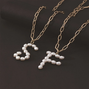 Close-up of golden necklaces with pearl-inlaid S and F letter pendants on black pedestals