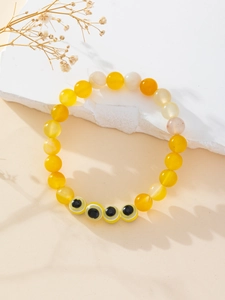 Close-up of yellow and white beaded bracelet with evil eye charms on a stone tray