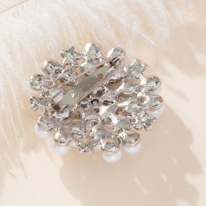 Elegant round pearl flower brooch with silver metal safety pin on feather background